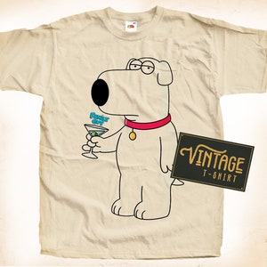 Puede incluir: Camiseta beige con un perro de dibujos animados sosteniendo una copa de martini. El perro lleva un collar rojo y gafas. El texto en la camiseta dice "Funky Guy" y también es visible una etiqueta de camiseta vintage.