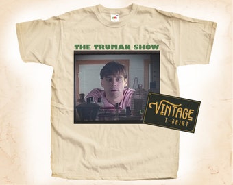 Könnte beinhalten: Cremefarbenes T-Shirt mit einem Grafikmotiv aus "The Truman Show". Das Design zeigt ein Standbild aus dem Film und den Text "THE TRUMAN SHOW" in Grün. Ein Etikett im Vintage-Stil ist ebenfalls vorhanden.