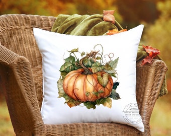 May include: White square pillow featuring a watercolor illustration of a large orange pumpkin with green leaves and vines. The pillow is placed on a wicker chair with a green blanket and autumn leaves in the background. The pillow has a Home Decor logo.