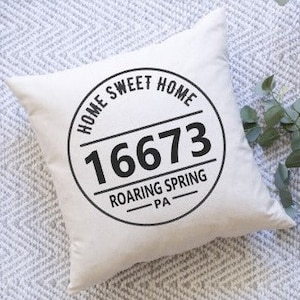 May include: Square, off-white pillow with a black circular design that reads "HOME SWEET HOME" around the top, "16673" in the center, and "ROARING SPRING PA" at the bottom. The pillow is on a patterned surface.