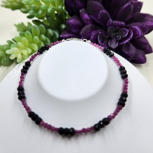 May include: A delicate bracelet made with alternating black and pink beads. The bracelet is made with small, round beads and has a silver clasp.