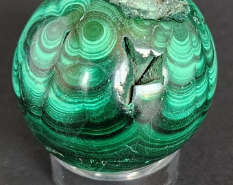 May include: A green malachite sphere with a swirling pattern, displayed on a clear stand.