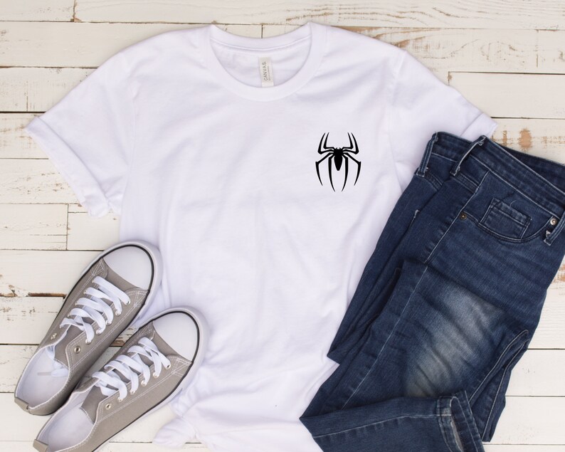 May include: White t-shirt with a black spider graphic on the front. The shirt is paired with gray sneakers and blue jeans.