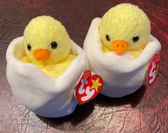 Peut inclure: Deux jouets en peluche de bébé poussin jaunes dans des nids en forme d'œuf blancs avec des étiquettes Ty beanie baby rouges et blanches. Les étiquettes ont une étoile blanche et les mots "Beanie Babies Baby".