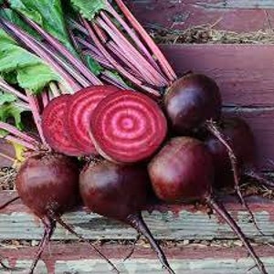 May include: A bunch of red beets with green leaves. Some of the beets are sliced in half, revealing the red flesh with white rings.