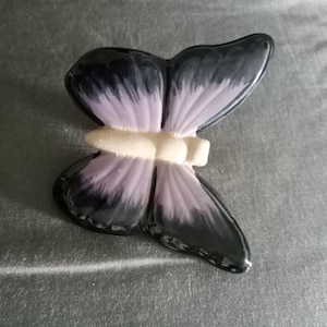 May include: A ceramic butterfly figurine with a glossy finish. The wings are a gradient of black and lavender, with a white body. The butterfly is resting on a gray surface.