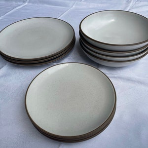 May include: A set of white ceramic plates and bowls with brown rims. The plates and bowls are stacked on top of each other.