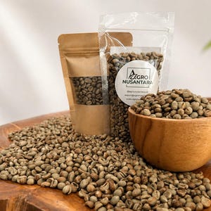 May include: A wooden bowl and two pouches filled with green coffee beans, with a scattering of beans on a wooden surface. One pouch is clear, displaying the beans, and has a label with text. The other pouch is brown.