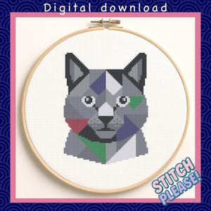 Könnte beinhalten: Ein Kreuzstichmuster eines geometrischen Katzenkopfes in Grau-, Blau-, Grün- und Rottönen, das in einem hölzernen Stickrahmen platziert ist. Die Wörter "Digital download" und "Stitch Please!" sind sichtbar.