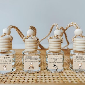 May include: Four glass bottles with wooden stoppers and string hangers. Each bottle has a different label with a humorous pet-themed scent description. The scents are "Puppy Breath", "Smells Like Kitty Biscuits", "In My Veterinarian Era", and "Fresh Scent of Cerenia".