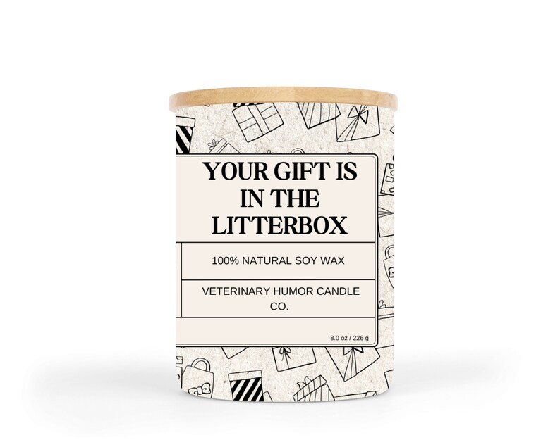 May include: A white candle jar with a black and white pattern of gift boxes. The jar has a wooden lid and a label that reads "Your gift is in the litterbox". The label also says "100% Natural Soy Wax" and "Veterinary Humor Candle Co.". The candle is 8 ounces or 226 grams.