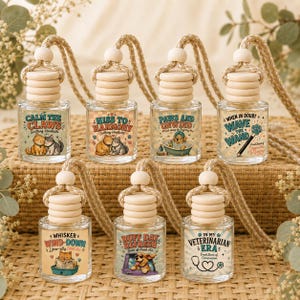 May include: Seven small glass car air freshener bottles with wooden caps and hanging ropes. Each bottle features a unique label with illustrations of cats or dogs and text including Calm the Claws, Hiss to Harmony, Paws and Unwind, Wave the Wand, Whisker Wind-Down, Ruff Day Refresh, and In My Veterinarian Era.