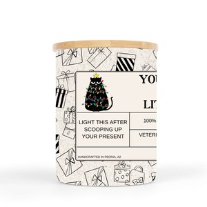 May include: A white candle jar with a black and white illustration of a cat sitting on a Christmas tree with lights. The text on the label reads "Light this after scooping up your present. 100% Soy Wax. Handcrafted in Peoria, AZ."