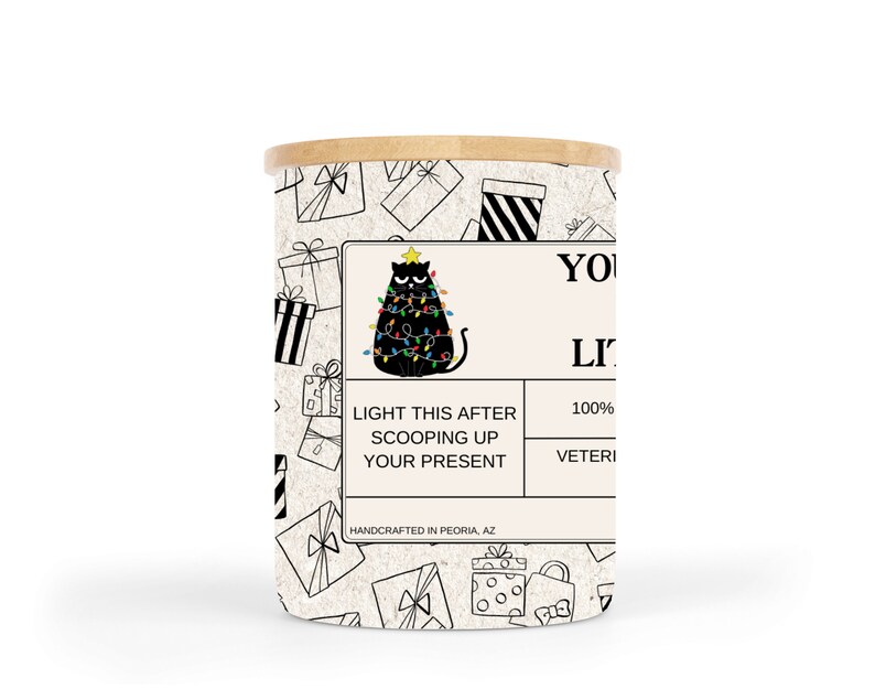 May include: A white candle jar with a black and white illustration of a cat sitting on a Christmas tree with lights. The text on the label reads "Light this after scooping up your present. 100% Soy Wax. Handcrafted in Peoria, AZ."