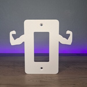 May include: White plastic light switch cover with a cutout of a bicep on each side.