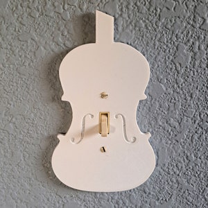 May include: White light switch cover shaped like a violin. The switch is in the off position.