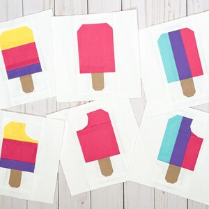 Könnte beinhalten: Sechs quadratische Papierbastelblöcke mit Eis am Stiel-Motiven. Drei Blöcke zeigen ganze Eis am Stiel in Gelb, Pink und Türkis-Lila-Pink. Drei Blöcke zeigen Eis am Stiel mit einem herausgebissenen Stück in ähnlichen Farbkombinationen.