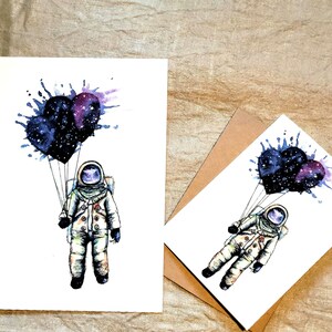 May include: A watercolor illustration of an astronaut holding three heart-shaped balloons. The balloons are filled with a galaxy pattern and are surrounded by watercolor splatters. The astronaut is wearing a white spacesuit with a blue visor.