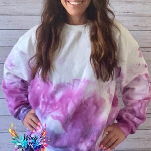 May include: A purple and white tie-dye sweatshirt with long sleeves. The sweatshirt has a relaxed fit and a crew neck.