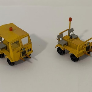 Peut inclure: Deux modèles réduits de véhicules jaunes. L'un a une cabine avec le numéro 162, l'autre est un véhicule en plein air avec le numéro 544. Les deux ont des roues noires, des sièges gris et des feux orange.