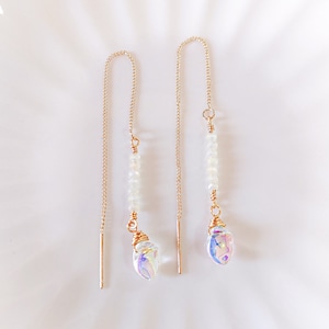 May include: A pair of gold chain earrings with iridescent teardrop crystals and white beads hanging from them.