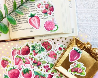 Può includere: Una collezione di adesivi di fragole colorati con vari disegni, tra cui fragole in un cestino, una tazza di fragole e una singola fragola. Gli adesivi sono su uno sfondo bianco con pois rosa.