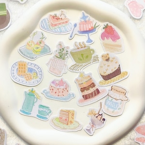 May include: A collection of colourful stickers featuring various designs, including cakes, pastries, teacups, and other whimsical illustrations. The stickers are arranged on a white plate and a white background.