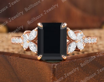 Könnte beinhalten: Ein Verlobungsring aus Roségold mit einem schwarzen Smaragdschliff-Edelstein und einem floralen Design mit kleineren Diamanten auf der Ringschiene.