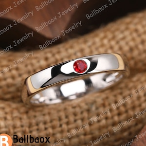 May include: A simple silver band ring with a single red gemstone set in the centre.