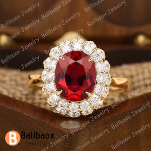 May include: A gold ring featuring a large oval red gemstone encircled by a halo of smaller white gemstones.