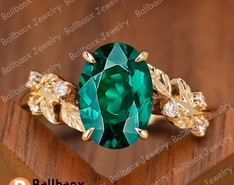 May include: A gold ring with a large oval green gemstone and a leaf design on the band. The ring is set with smaller clear gemstones on the band.