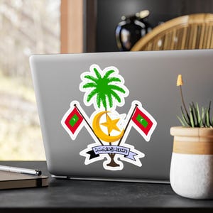 May include: A sticker featuring the coat of arms of the Maldives. The design includes a green palm tree, a crescent moon and star, and two flags with a red background and a green crescent. The sticker is applied to a laptop.