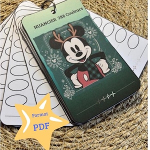 Peut inclure: Un ensemble de cartes d'échantillons de couleurs avec Mickey Mouse portant des bois de renne et une veste à carreaux. Les cartes sont reliées par un anneau métallique. Le texte "NUANCIER 288 Couleurs" est en haut. Une étoile jaune avec "Format PDF" est en bas à gauche.