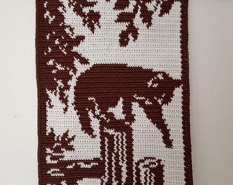 Puede incluir: Un tapiz de pared hecho a mano con un diseño de gato marrón y blanco. El gato está posado en un tocón de árbol, rodeado de hojas y ramas. El tapiz rectangular está colgado de una barra de madera.