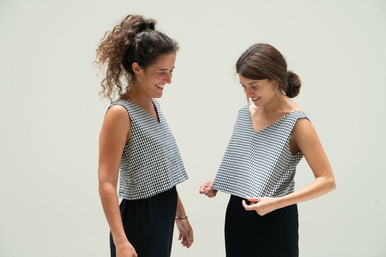 May include: Two sleeveless tops with a black and white houndstooth pattern and a V-neck. The tops are paired with black bottoms. The image shows two people wearing the tops, smiling.