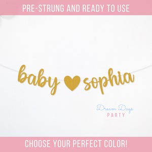 May include: Gold glitter baby shower banner with the text "baby sophia" and a heart in between the words. The banner is pre-strung and ready to use.