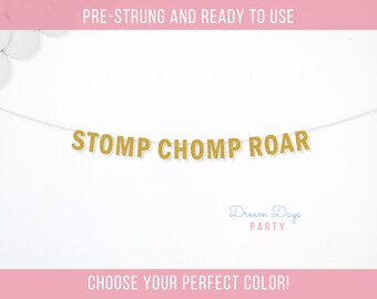 May include: A gold glitter banner with the words "STOMP CHOMP ROAR" strung across a white background. The banner is pre-strung and ready to use. The text "Dream Days PARTY" is below the banner. The text "CHOOSE YOUR PERFECT COLOR!" is at the bottom.