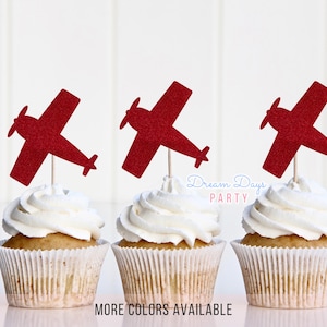 May include: Three cupcakes with white frosting and red airplane toppers. The cupcakes are in white paper liners. The image has the text "Dream Days Party" and "MORE COLORS AVAILABLE".