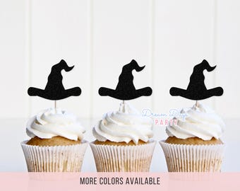 May include: Three cupcakes with white frosting, each topped with a black glittery witch hat cupcake topper on a thin wooden pick. The text Dream Days PARTY is visible in light blue and pink, and the text MORE COLORS AVAILABLE is at the bottom.