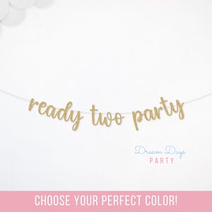 May include: A gold glitter banner that reads "ready two party" on a white string. The banner is against a white background with white balloons in the upper left corner. The text "Dream Days Party" is below the banner.