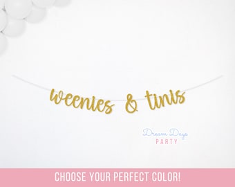 May include: A gold glitter banner featuring the cursive text weenies & tinis strung on a thin white cord. The banner is displayed against a white background with white balloons in the upper left corner and the text Dream Days PARTY below.