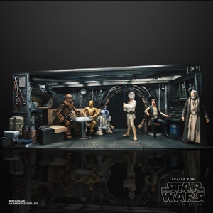 Op de afbeelding: Een gedetailleerd diorama met Star Wars-actiefiguren in een interieursetting. De scène toont Chewbacca, C-3PO, R2-D2, Luke Skywalker, Han Solo en Obi-Wan Kenobi. De set is donker met metalen accenten. De tekst "SCALED FOR STAR WARS" is zichtbaar.