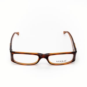 Op de afbeelding: Rechthoekige bruine en bruingele bril met de merknaam "VOGUE" op het rechterglas. De monturen hebben een schildpadpatroon. De bril staat tegen een witte achtergrond.