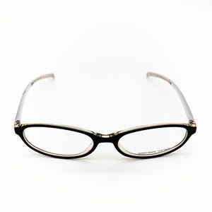 Könnte beinhalten: Brille mit ovalem, schwarzem Rahmen und silberfarbenen Bügeln. Die Gläser sind klar. Der Text "HAND MADE ACETATE" ist auf dem unteren rechten Glas aufgedruckt. Auf weißem Hintergrund.