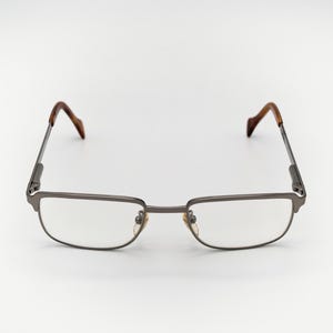 Puede incluir: Un par de gafas de metal plateado con lentes transparentes. Las patillas de las gafas son marrones.