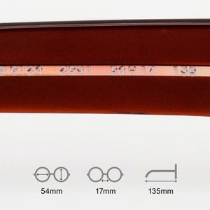 May include: Close-up of the inner frame of eyeglasses. The frame is a dark reddish-brown colour with a thin, metallic gold-coloured strip. The text "RB 6124 2531 59 17 135" is printed on the gold strip. The image includes diagrams with measurements: 54mm, 17mm, and 135mm.