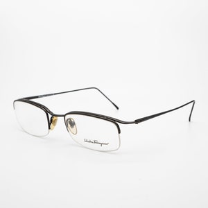 May include: A pair of black metal eyeglasses with a half-rim design. The glasses have clear lenses and the brand name "Salvatore Ferragamo" is printed on the right temple.