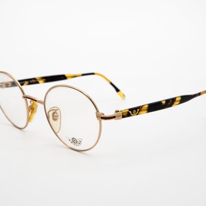 May include: Round gold-tone eyeglasses with tortoiseshell arms. The arms feature a gold-tone logo.