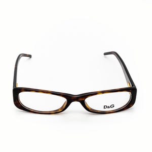 Könnte beinhalten: Brille mit einem Schildpattmuster-Rahmen und klaren Gläsern. Das D&G-Logo ist auf dem rechten Glas sichtbar. Die Brille hat eine rechteckige Form mit abgerundeten Kanten und dunkelbraunen Bügeln.