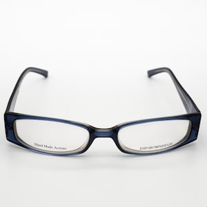 May include: Blue rectangular eyeglasses with clear lenses. The left lens has the text "Hand Made Acetate" and the right lens has the text "EMPORIO ARMANI".